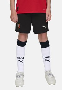 Mustad mustritooted lühikesed püksid Puma logoga, punane jersy, valged põlvikud, millel on "1901" ja Puma logo, ning hõbedased spordijalatsid.