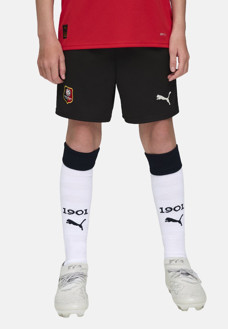 Mustad mustritooted lühikesed püksid Puma logoga, punane jersy, valged põlvikud, millel on "1901" ja Puma logo, ning hõbedased spordijalatsid.