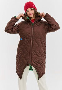 Hnedý prešívaný dlhý kabát so zelenými akcentmi a vysokým golierom. Obsahuje zipové zapínanie a dve bočné vrecká. Tkanina vyzerá hladko a nadýchnuto.