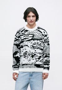 Jersey de punto en blanco y negro, con patrones abstractos, textura gruesa y cuello redondo con puños y dobladillo acanalados.