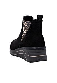 Bottine en suede noir avec un panneau latéral en élastique à motif léopard et une semelle en coin moderne, présentant un léger éclat sur le matériau.
