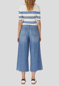 Lichtblauwe brede denim culottes met een hoge taille, voorzien van twee achterzakken en een rafelige zoom. Gecombineerd met een wit en blauw gestreept shirt.