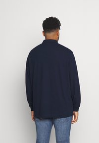 Polo-shirt à manches longues bleu marine avec un col, en tissu doux, présentant une coupe droite et une silhouette décontractée, ample.