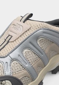 Πεζοπορικό παπούτσι από ανάλαφρο πλέγμα σε μπεζ και γκρι χρώμα, με λουρί έλξης, λογότυπο και ανθεκτική εξωτερική σόλα.