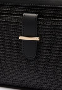 Black woven handbag featuring a textured surface, black leather strap, and a gold-tone metal accent for closure.