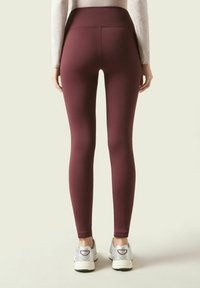 Leggings burdeos con cintura alta, hechos de material elástico, diseño ajustado, combinados con zapatillas deportivas plateadas.