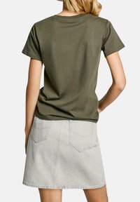 Camiseta de algodón verde oliva de manga corta combinada con una falda de mezclilla gris claro que presenta dos bolsillos traseros y un corte recto.