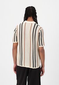 Strickhemd mit kurzen Ärmeln in Creme mit vertikalen Streifen in Schwarz, Orange und Braun. Es hat einen spitzen Kragen und einen strukturierten Stoff.