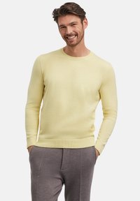 Maglione a collo rotondo di un giallo chiaro in maglia, con polsini e orlo a coste, abbinato a pantaloni grigi con texture. Tessuto liscio, design aderente.