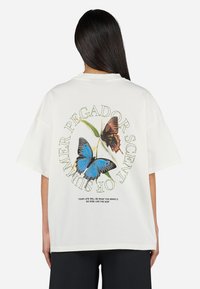 Camiseta de algodón blanca con un gran gráfico de mariposa en azul y marrón en la parte posterior, con texto verde que dice "PEGADOR AROMA DE VERANO."