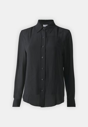 Crna košulja na dugih rukava od glatkog materijala, s klasičnim ovratnikom, dugim rukavima i vertikalnim šavovima.