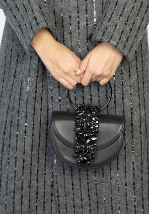 Sac à main en cuir noir de forme arrondie, avec une poignée texturée ornée de grandes pierres précieuses noires. Porté avec un vêtement gris à paillettes.