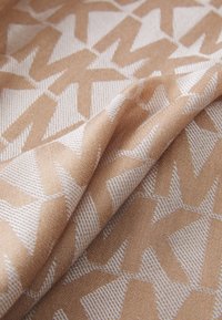 Ett mönstrat tyg med en geometrisk design i jordnära toner av beige och ljusbrunt, med texturerade, vävda detaljer.