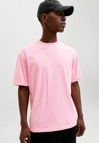 Roosa puuvillane t-särk ümarate kaelusega ja lühikeste varrukatega. Kergelt lõdvestunud lõige, sile pind, ilma nähtavate mustrite või dekoratsioonideta.