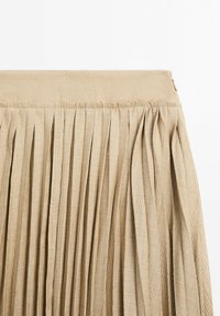 Rypistetty vaaleanbeige hame, joka on valmistettu teksturoidusta kankaasta, jossa on sileä vyötärö ja hienot yksityiskohdat. Ominaisuutena pystysuorat laskokset, jotka lisäävät syvyyttä.