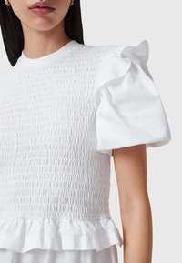 Top blanco con textura fruncida y mangas cortas acampanadas. El torso es ajustado, con un dobladillo acampanado en la cintura.