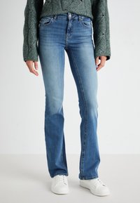 Light blue denim flared jeans with a mid-rise waist, five pockets, contrast stitching, and a hint of wear at the knees. Paired with white sneakers.