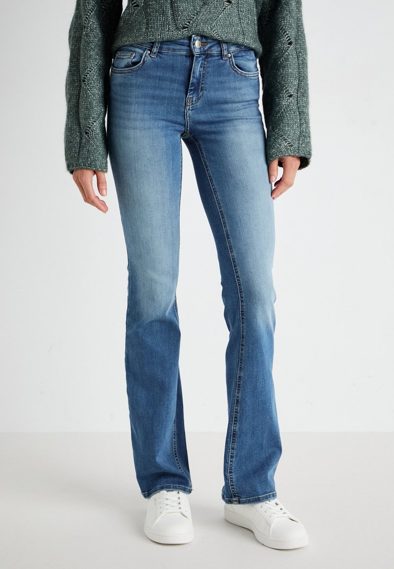 Lichtblauwe denim flare jeans met een middelhoge taille, vijf zakken, contrasterende stiksels en een beetje slijtage bij de knieën. Gecombineerd met witte sneakers.