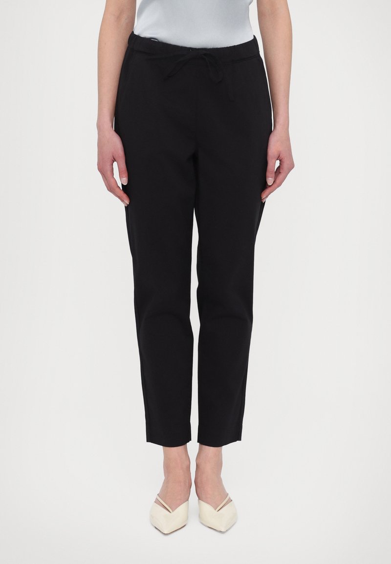 Black, tapered trousers with an elastic waistband and drawstring. Smooth fabric with a slim fit, ending just above the ankle.