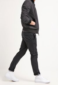 Zwarte gewatteerde bomberjack met geribbelde manchetten, gecombineerd met donkere broek en witte high-top sneakers. Eenvoudig, eigentijds ontwerp.