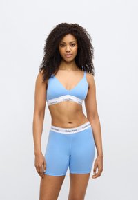 Ανοιχτό μπλε βαμβακερό σουτιέν bralette με ρυθμιζόμενους ιμάντες και λευκή ταινία "Calvin Klein"· συνδυασμένο με αντίστοιχα μπλε βαμβακερά σορτς, επίσης με λωρίδα λογότυπου.