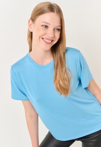 Lichtblauw t-shirt met korte mouwen van zacht materiaal met een ronde halslijn. Het heeft een losvallende pasvorm en subtiele stikseldetails.