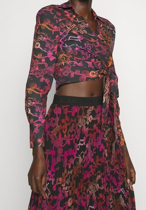 Cropped long-sleeve blouse and pleated skirt with pink, orange, and brown intricate chain and key pattern on black fabric.
