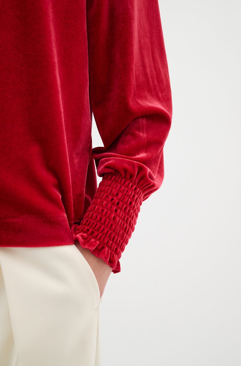 Rotes Samt-Oberteil mit langen Ärmeln und gerafftem Strick an den Manschetten, mit einem glatten Körper und einer lockeren Passform, kombiniert mit cremefarbener Hose.