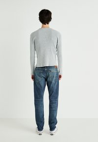 Jasnoszara, prążkowana koszula z długim rękawem w połączeniu z niebieskimi dżinsami; koszula ma prosty dół, a dżinsy mają tylne kieszenie oraz widoczną metkę marki.