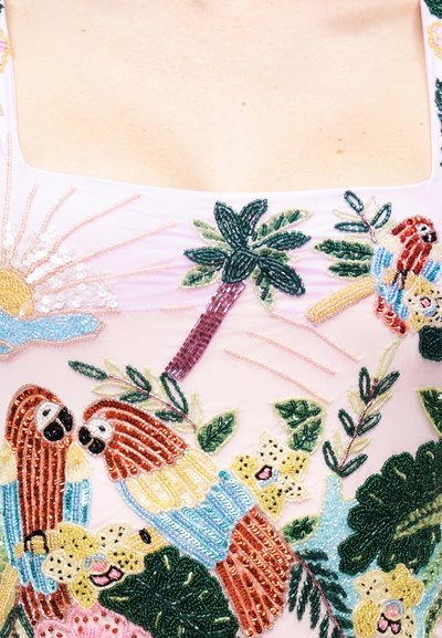 Κοντινό πλάνο με διακοσμητικό σχέδιο από χάντρες σε ανοιχτό ροζ ύφασμα που απεικονίζει παπαγάλους, φοίνικα, ήλιο και πολύχρωμα λουλούδια.