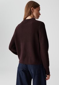 Pull en maille bourgogne avec une texture côtelée, col rond et épaules tombantes, associé à un jean large bleu foncé.