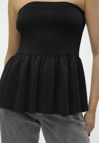 Svart strapless topp i ribbat tyg med en utställd peplumdesign. Pairad med grå högmidjade jeans som framhäver midjan.
