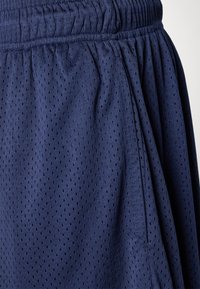 Marineblaue Sportshorts aus leichtem, atmungsaktivem Mesh-Gewebe mit kleinen Perforationen, ausgestattet mit einem elastischen Bund und seitlichen Taschen.
