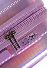 Valise rigide violette avec une surface texturée, double zippers, un verrou à combinaison et un motif de rayures horizontales distinctif.
