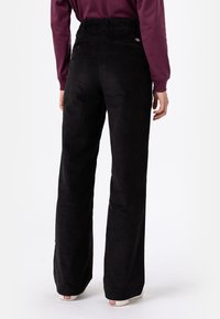 Pantalones de pana negra con un diseño de pierna recta, que presentan una cintura alta, bolsillos traseros y un acabado texturizado.