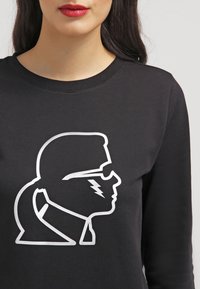 Černá mikina se výraznou bílou grafickou siluetou profilu s brýlemi a akcenty v podobě blesků. Měkká tkanina a klasický střih.