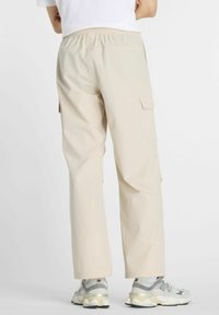 Pantalones cargo beige con cinturilla elástica y bolsillos laterales. El material parece suave y ligero, combinados con zapatillas grises y blancas.