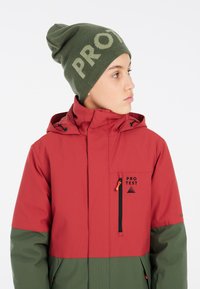 Rote und grüne wasserdichte Jacke mit Kapuze, ausgestattet mit schwarzem Zubehör, Reißverschlusstaschen und einem Logo. Strickmütze in Grün mit "PRO"-Text.
