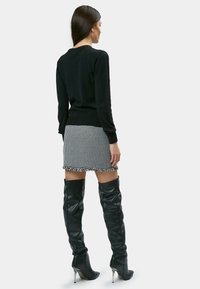 Schwarzer Strickpullover, Hahnentrittmuster-Minirock mit fransigem Saum und knielange schwarze Lederstiefel mit spitzen silbernen Absätzen.