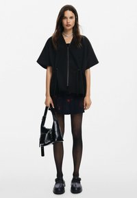 Top nera con zip e maniche corte, abbinato a una gonna scura con fiori, calze trasparenti e scarpe chunky nere. Accessoriato con una borsa nera.