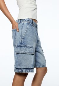 Shorts cargo en denim, bleu clair avec une finition délavée. Ils disposent de poches latérales, d'un ourlet effiloché et d'une coupe décontractée.