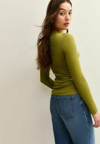 Green ribbed long-sleeve top paired with blue high-waisted jeans, featuring a tailored fit and subtle texture, shown from a slight angle.