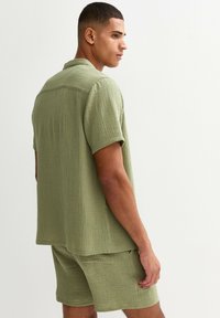 Camicetta verde a maniche corte con pantaloni abbinati, caratterizzata da una vestibilità rilassata e un sottile motivo sgualcito. Design del colletto semplice.