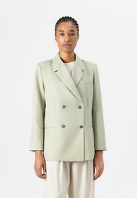 Dobbeltspent blazer i lys grønn stoff, med notched krage, to knapper og brystlomme. Strukturert design med glatt tekstur.