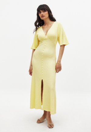 Žlté midi šaty s textúrou, V-výstrihom, krátkymi rukávmi, gombíkovými detailmi na prednej strane a s predným rozparkom. Klasický dizajn s priliehavým strihom.