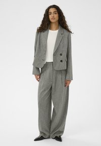 Sivi vzorčasti dvoredni blazer z velikimi gumbi, kombiniran z ujemajočimi ohlapnimi hlačami in belo majico; gladka tekstura tkanine.