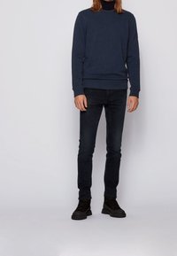 Sudadera azul marino de manga larga, cuello redondo y puños acanalados, combinada con jeans de mezclilla negros y botas negras con cordones.