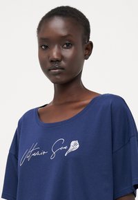 Navyblauwe t-shirt van zachte katoen. Heeft een ronde halslijn en korte mouwen. Op de voorkant staat de tekst "Vitamin Sea" en een schelpafbeelding in het wit.