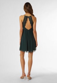 Mörkgrön chiffongklänning med detaljer i spets på ryggen, ärmlös design och utsvängd kjol, med öppen rygg och justerbara remmar.