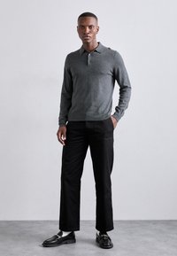 Grå langermet polo-skjorte med krage, kombinert med svarte rettsydde bukser og svarte loafers med dekorative metallbeslag.